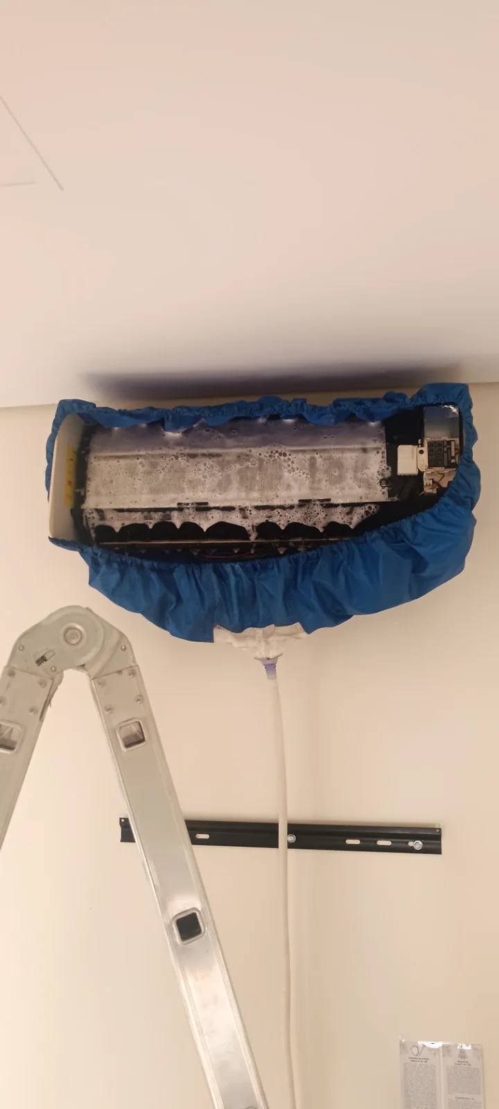 Equipamento de ar-condicionado aberto com capa de proteção durante limpeza e higienização.