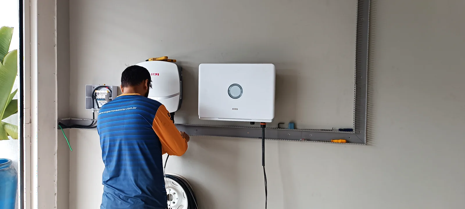 Técnico instalando inversor e acabamento elétrico em parede técnica.