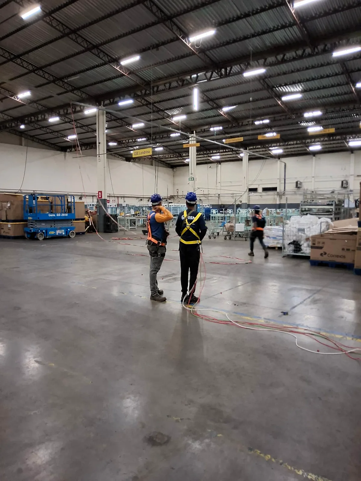 Equipe da GSM com EPIs e cinto de segurança executando infraestrutura elétrica em galpão industrial de grande porte.