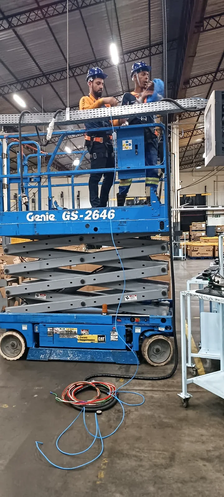 Técnicos da GSM sobre plataforma elevatória executando infraestrutura aérea e cabeamento em ambiente industrial.