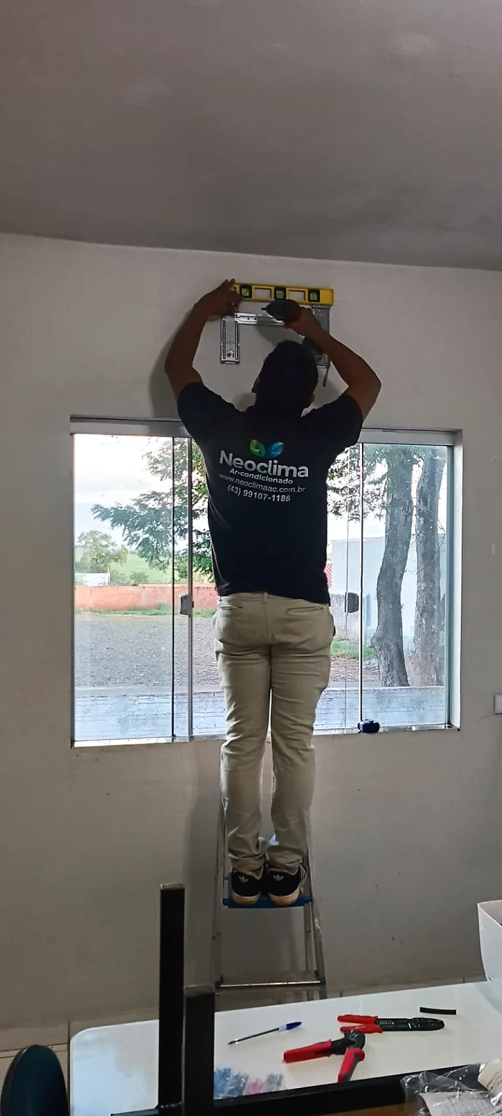 Técnico da Neoclima sobre escada preparando a instalação de equipamento de ar-condicionado em parede.