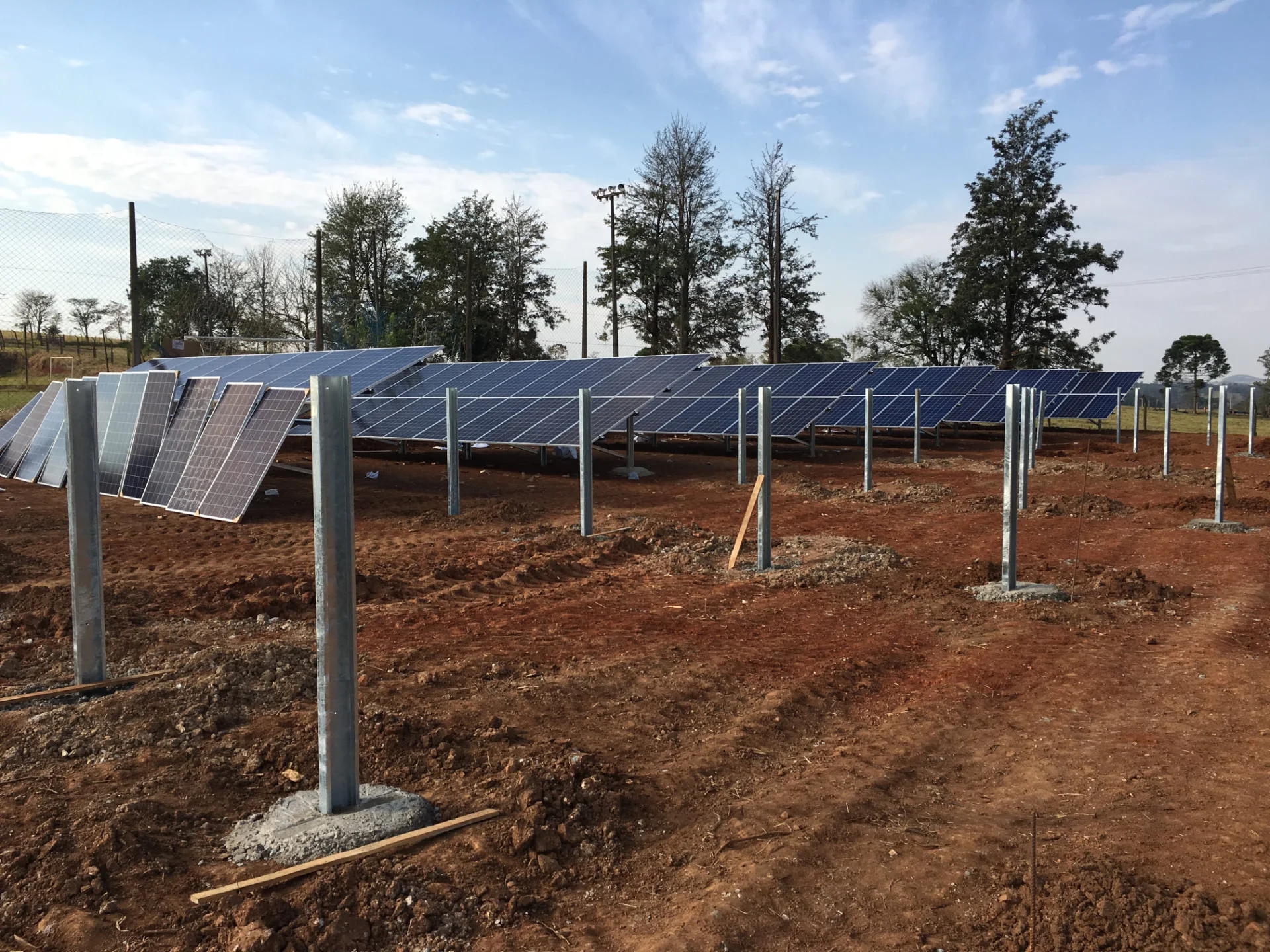 Usina solar em solo em área rural, com fileiras de módulos fotovoltaicos sobre estruturas metálicas galvanizadas em montagem.
